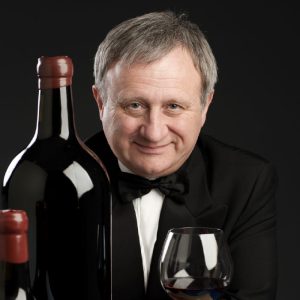 Dottor Giuseppe Vaccarini, miglior sommelier del mondo e docente collaboratore dell’Agenzia Formativa Dante Alighieri, in smoking con calice di vino rosso e bottiglie.