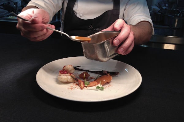 Lo chef stellato Andrea Berton rifinisce un piatto in cucina con attenzione al dettaglio e alla presentazione.