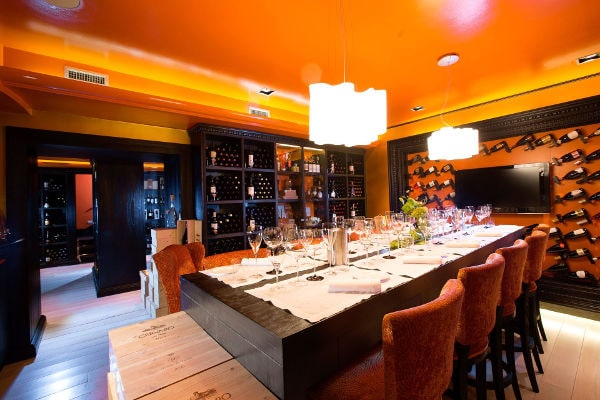 Cantina di Casa Vissani con arredo moderno, pareti arancioni e tavolo degustazione circondato da bottiglie di vino.