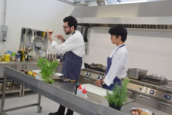 Lo chef Fabrizio Ferrari in cucina durante una lezione pratica con un allievo, dimostrazione tecnica di alta ristorazione.