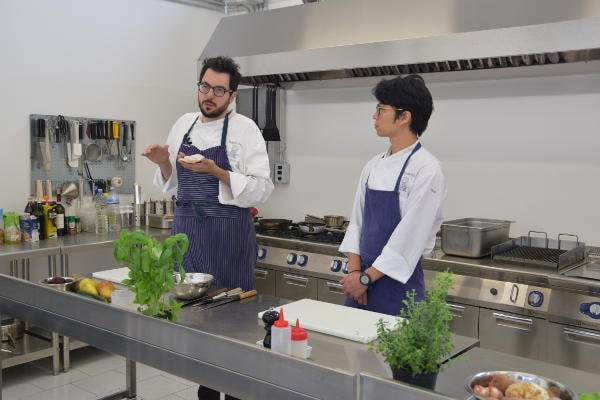 Lo chef Fabrizio Ferrari spiega una preparazione a un allievo in cucina, lezione del corso di alta ristorazione.