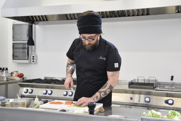 Chef Gionata Bignotti taglia il salmone durante una lezione pratica di cucina professionale.
