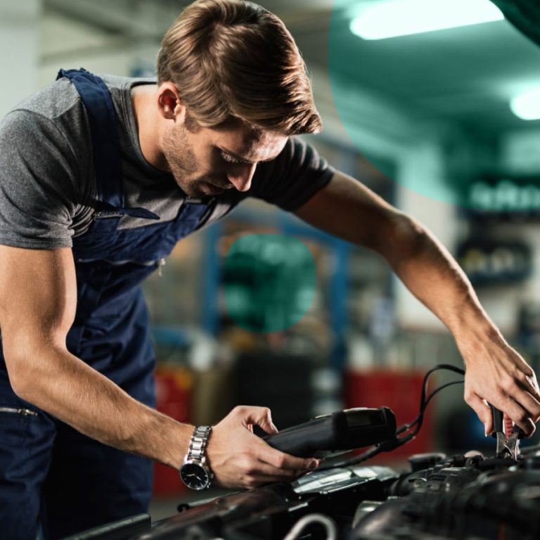 Elettrauto con tuta da lavoro controlla il motore di un’auto utilizzando strumenti diagnostici in officina.