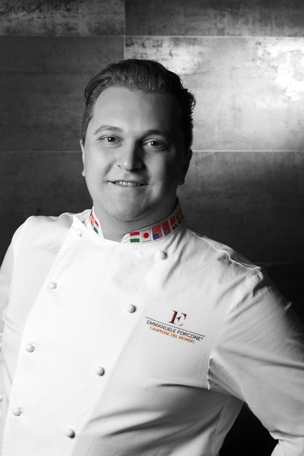 Emmanuele Forcone, campione del mondo di pasticceria e docente Dante Alighieri, in giacca da chef bianca con colletto decorato dalle bandiere internazionali.