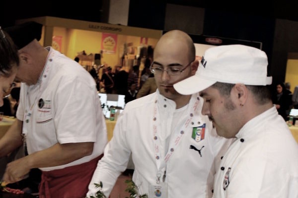 Il maestro pizzaiolo Giuseppe Lapolla mentre prepara ingredienti con colleghi durante un evento di gara internazionale.