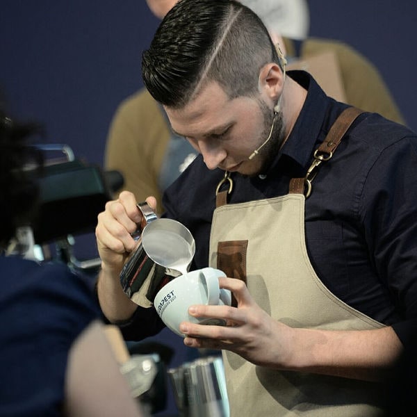 Matteo Beluffi durante una dimostrazione di latte art, versa il latte con precisione in una tazza davanti al pubblico.