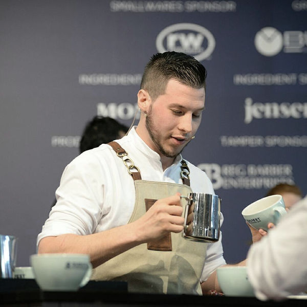 Matteo Beluffi concentra l’attenzione su una tazza di cappuccino mentre perfeziona una tecnica di latte art sul palco.
